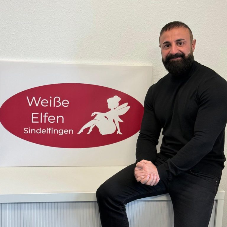 Der Geschäftsführer sitzt neben einem Schild mit der Aufschrift "Weiße Elfen".